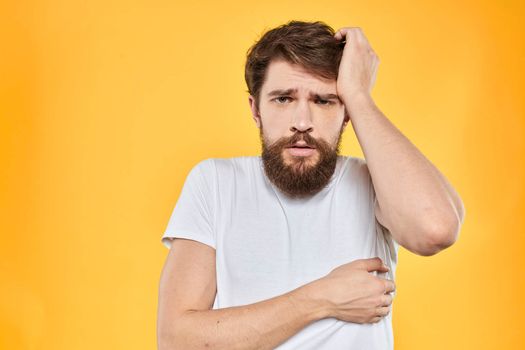 Man in white t-shirt emotions studio gestures with hands displeased facial expression yellow background. High quality photo