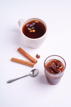 Hot black aromatic tea near to fig jam, Christmas breakfast mood with anise and cinnamon on white background, angle view