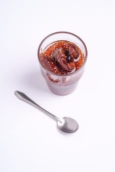 Fig jam in glass with spoon, breakfast mood fruit food on white background, angle view