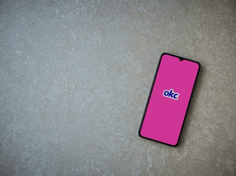 Lod, Israel - July 8, 2020: OkCupid app launch screen with logo on the display of a black mobile smartphone on ceramic stone background. Top view flat lay with copy space.