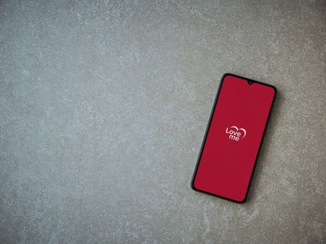 Lod, Israel - July 8, 2020: Loveme app launch screen with logo on the display of a black mobile smartphone on ceramic stone background. Top view flat lay with copy space.