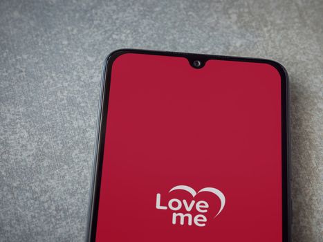 Lod, Israel - July 8, 2020: Loveme app launch screen with logo on the display of a black mobile smartphone on ceramic stone background. Top view flat lay with copy space.