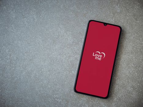 Lod, Israel - July 8, 2020: Loveme app launch screen with logo on the display of a black mobile smartphone on ceramic stone background. Top view flat lay with copy space.