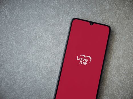 Lod, Israel - July 8, 2020: Loveme app launch screen with logo on the display of a black mobile smartphone on ceramic stone background. Top view flat lay with copy space.