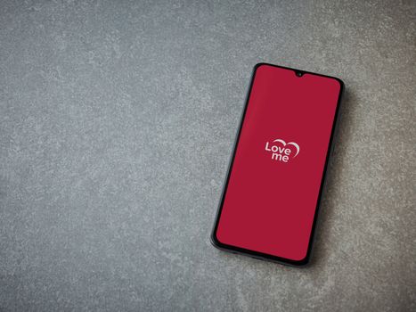 Lod, Israel - July 8, 2020: Loveme app launch screen with logo on the display of a black mobile smartphone on ceramic stone background. Top view flat lay with copy space.