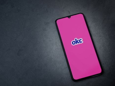 Lod, Israel - July 8, 2020: OkCupid app launch screen with logo on the display of a black mobile smartphone on dark marble stone background. Top view flat lay with copy space.