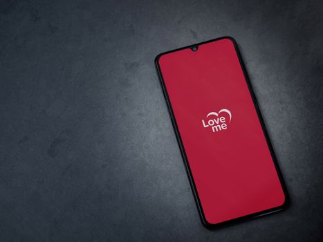 Lod, Israel - July 8, 2020: Loveme app launch screen with logo on the display of a black mobile smartphone on dark marble stone background. Top view flat lay with copy space.