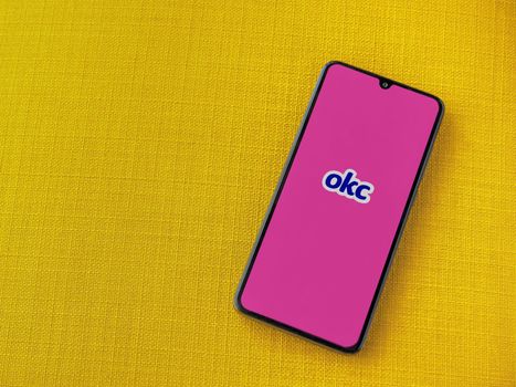 Lod, Israel - July 8, 2020: OkCupid app launch screen with logo on the display of a black mobile smartphone on a yellow fabric background. Top view flat lay with copy space.