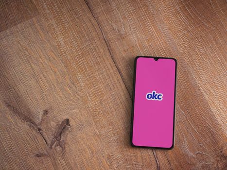 Lod, Israel - July 8, 2020: OkCupid app launch screen with logo on the display of a black mobile smartphone on wooden background. Top view flat lay with copy space.