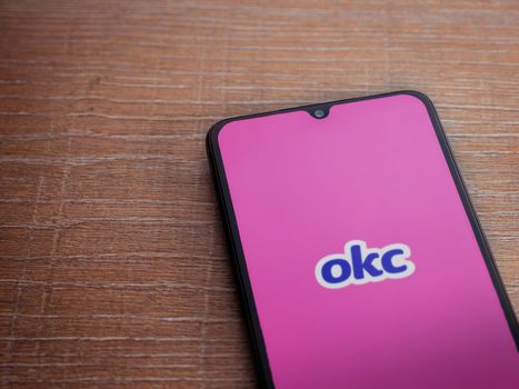 Lod, Israel - July 8, 2020: OkCupid app launch screen with logo on the display of a black mobile smartphone on wooden background. Top view flat lay with copy space.