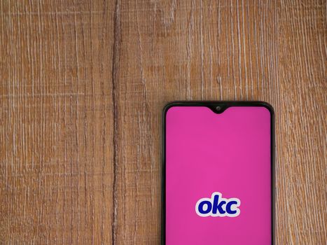 Lod, Israel - July 8, 2020: OkCupid app launch screen with logo on the display of a black mobile smartphone on wooden background. Top view flat lay with copy space.