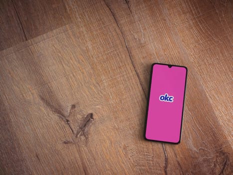 Lod, Israel - July 8, 2020: OkCupid app launch screen with logo on the display of a black mobile smartphone on wooden background. Top view flat lay with copy space.
