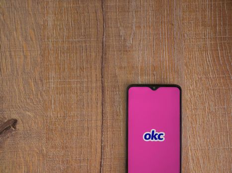 Lod, Israel - July 8, 2020: OkCupid app launch screen with logo on the display of a black mobile smartphone on wooden background. Top view flat lay with copy space.