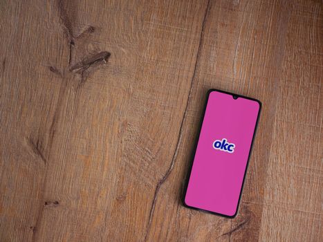 Lod, Israel - July 8, 2020: OkCupid app launch screen with logo on the display of a black mobile smartphone on wooden background. Top view flat lay with copy space.