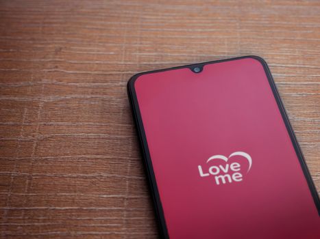 Lod, Israel - July 8, 2020: Loveme app launch screen with logo on the display of a black mobile smartphone on wooden background. Top view flat lay with copy space.