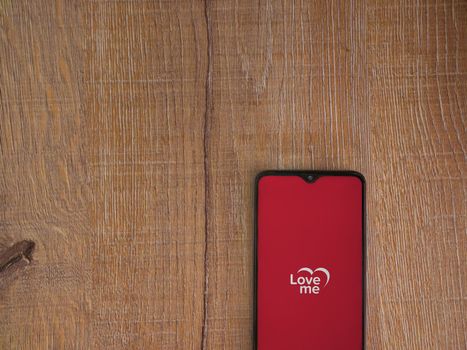 Lod, Israel - July 8, 2020: Loveme app launch screen with logo on the display of a black mobile smartphone on wooden background. Top view flat lay with copy space.