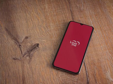 Lod, Israel - July 8, 2020: Loveme app launch screen with logo on the display of a black mobile smartphone on wooden background. Top view flat lay with copy space.