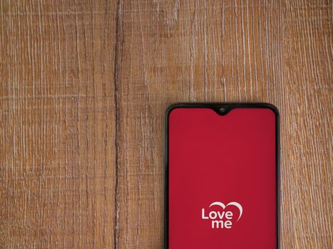 Lod, Israel - July 8, 2020: Loveme app launch screen with logo on the display of a black mobile smartphone on wooden background. Top view flat lay with copy space.