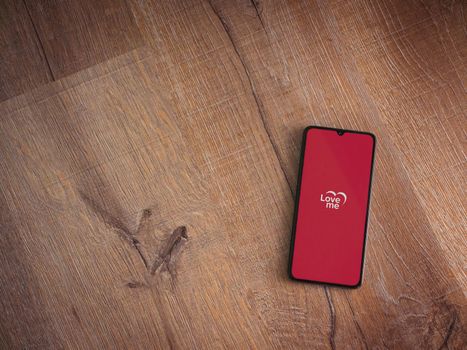 Lod, Israel - July 8, 2020: Loveme app launch screen with logo on the display of a black mobile smartphone on wooden background. Top view flat lay with copy space.