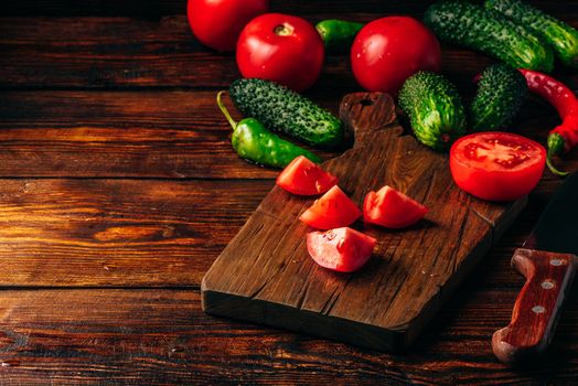 Sliced tomatoes on cutting board and cucumbers with chili peppers over wooden background.