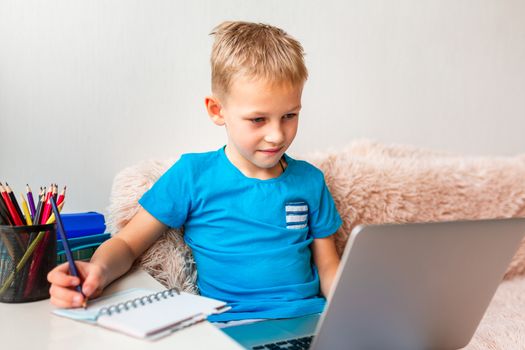 Little young school boy working at home with a laptop and class notes studying in a virtual class. Distance education and learning, e-learning, online learning concept during quarantine