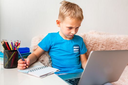 Little young school boy working at home with a laptop and class notes studying in a virtual class. Distance education and learning, e-learning, online learning concept during quarantine