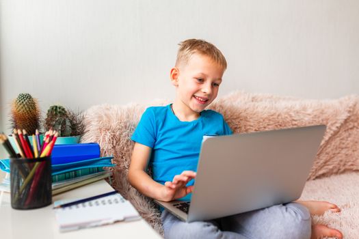 Little young school boy working at home with a laptop and class notes studying in a virtual class. Distance education and learning, e-learning, online learning concept during quarantine