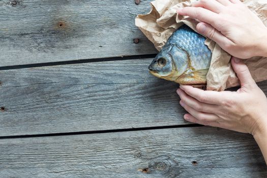 Hand holds Dried Volga bream vobla in a crumpled kraft paper roll, delicious beer snack, close-up.