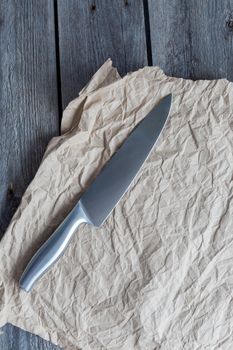 sharp knife on crumpled craft paper on wooden background, copy space.