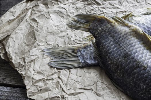 Salted Dry fish vobla on crumpled craft paper on wooden background, delicious beer snack, close-up.