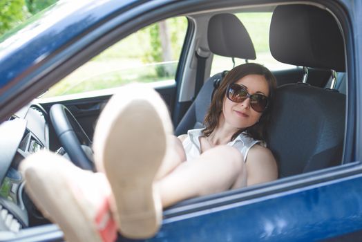 Adult woman with sunglasses lying inside her car. Woman enjoying on a road trip.