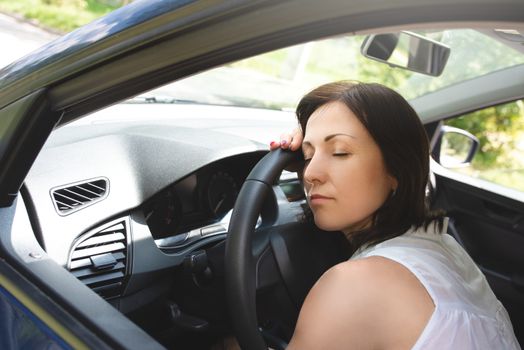 Tired woman asleep on steering wheel in her car