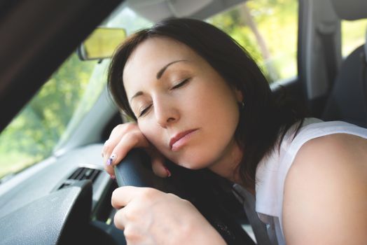 Tired woman asleep on steering wheel in her car