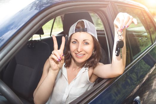 Beautiful woman in a hat holding keys to new bought car and smiling at camera in summer sunny day. Woman drives a car