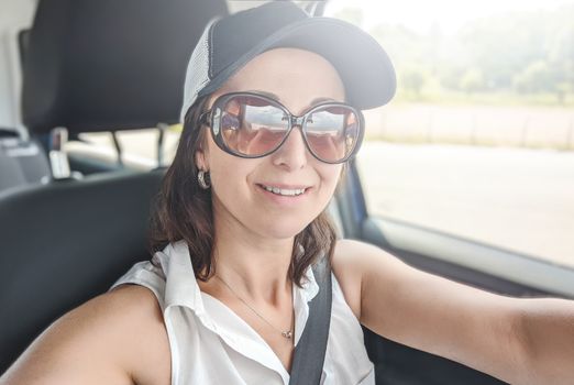 Attractive young woman making selfie on her smartphone. Female in the car making a photo shot on her cell phone.