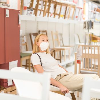 New normal during covid epidemic. Caucasian woman shopping at retail furniture and home accessories store wearing protective medical face mask to prevent spreading of corona virus.