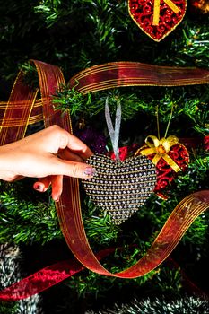 Hand putting heart shaped Christmas decorations on fir branches decorating Christmas tree, Christmas hanging decorations.