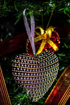 Hand putting heart shaped Christmas decorations on fir branches decorating Christmas tree, Christmas hanging decorations.