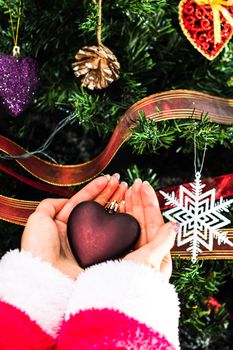 Hands holding Christmas ornament in front of Christmas tree. Decorating fir branches with Christmas decorations.