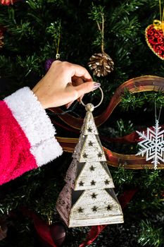 Hands holding Christmas ornament in front of Christmas tree. Decorating fir branches with Christmas decorations.