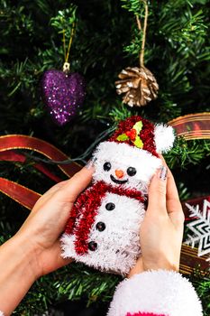 Hands holding Christmas snowman figurine in front of the Christmas tree. Decorating the fir tree isolated