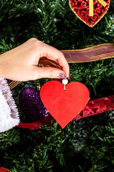 Decorating Christmas tree, hand putting Christmas decorations on fir branches. Christmas hanging decorations.