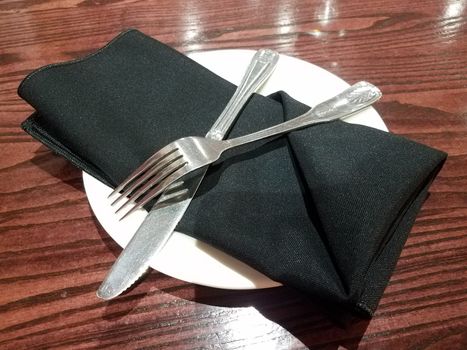 fork and knife and black napkin on plate on wood table