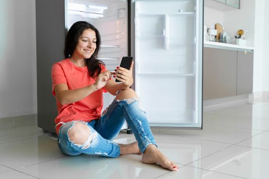 A girl orders food using a smartphone. Empty refrigerator with no food. Food delivery service advertisement.