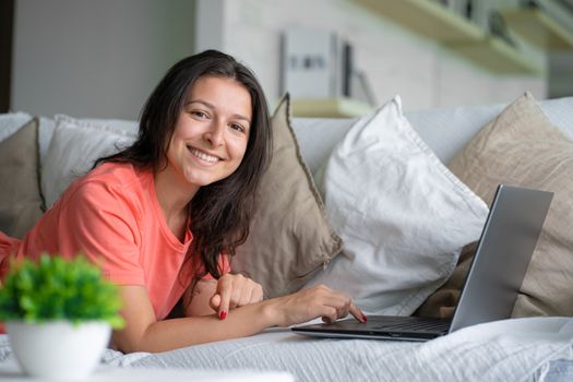 Girl lying on the couch rejoices looking at the laptop. Smiles, good mood, emotion of joy.