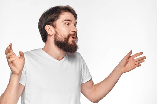 cheerful bearded man in a white t-shirt emotions gestures with his hands light background studio. High quality photo