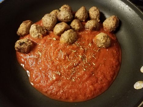 red tomato sauce in frying pan or skillet with herbs with meatballs