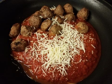 red tomato sauce in frying pan or skillet with herbs with meatballs and cheese