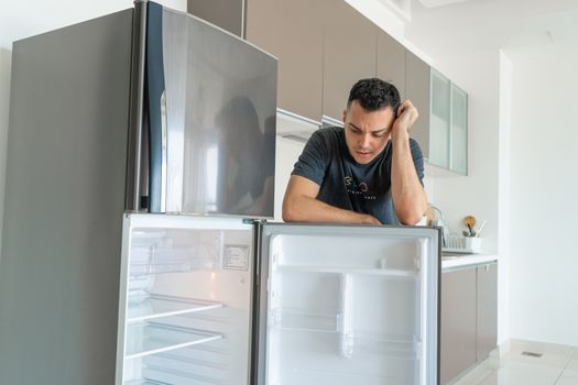 The guy is sad near the empty refrigerator without food. Food delivery service advertisement.