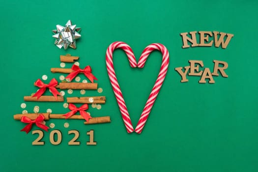 Christmas composition 2021 cinnamon tree, red bows, candy, Christmas cane candies on a green background. Christmas, winter, new year concept. Flat lay, top view, copy space
